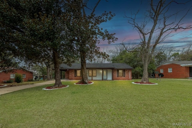 view of front of property with brick siding, driveway, and a yard