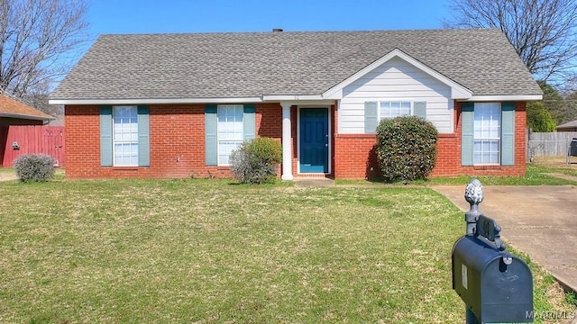 view of front facade with brick siding, a shingled roof, a front lawn, and fence