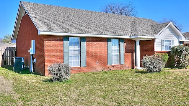 view of front of property featuring a front yard, brick siding, central AC, and a shingled roof