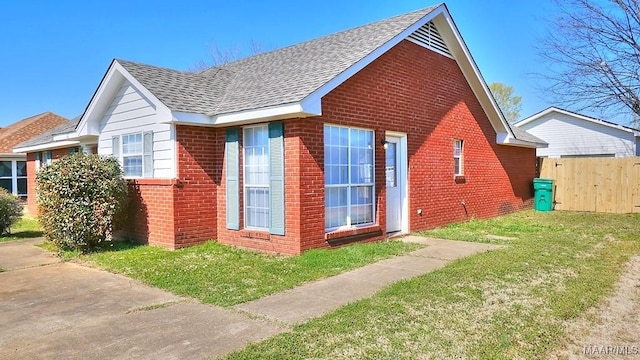 view of side of property with a yard, fence, brick siding, and roof with shingles