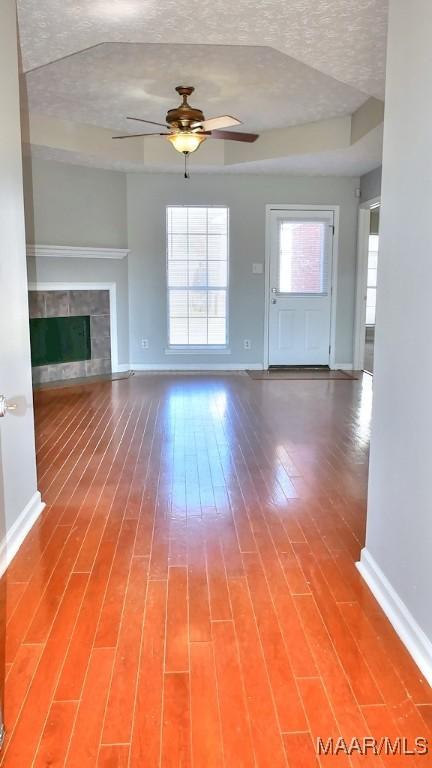 unfurnished living room with wood finished floors, baseboards, a fireplace, ceiling fan, and a textured ceiling