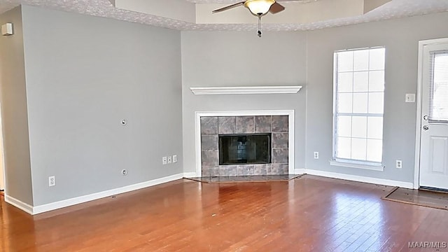 unfurnished living room with a fireplace, wood finished floors, baseboards, and ceiling fan