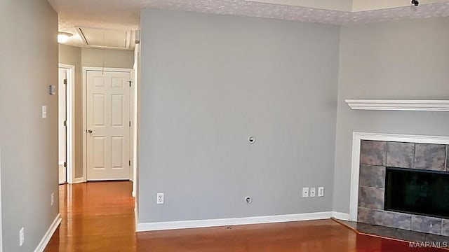 unfurnished living room with attic access, wood finished floors, a fireplace, and baseboards