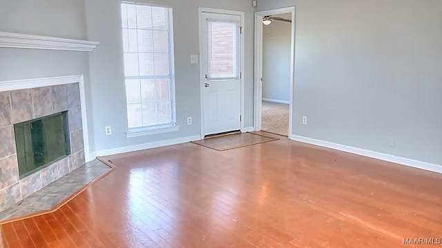 unfurnished living room with a tiled fireplace, a ceiling fan, baseboards, and wood finished floors