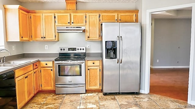 kitchen with stone finish floor, under cabinet range hood, a sink, appliances with stainless steel finishes, and light countertops