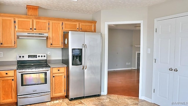 kitchen with under cabinet range hood, a textured ceiling, appliances with stainless steel finishes, light countertops, and baseboards