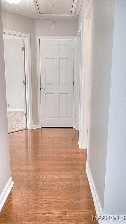 hallway with attic access, light wood-style flooring, and baseboards