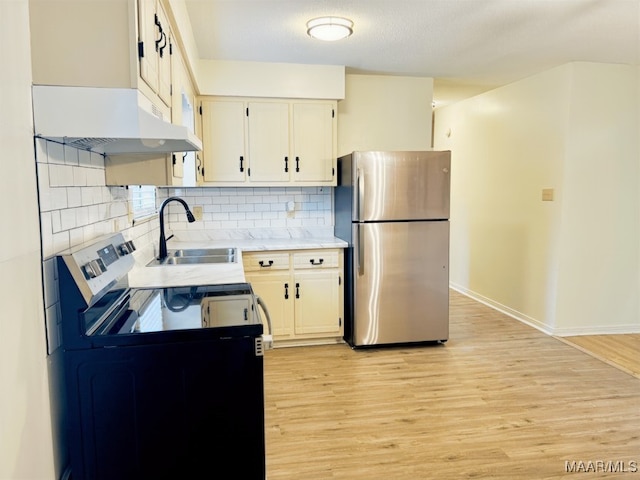 kitchen with backsplash, light wood finished floors, freestanding refrigerator, and a sink