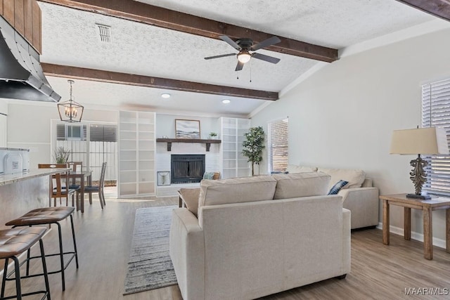 living area featuring visible vents, ceiling fan with notable chandelier, a textured ceiling, a fireplace, and light wood finished floors