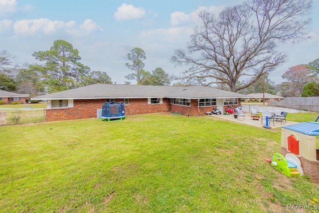 rear view of property with fence, a lawn, a trampoline, a patio area, and brick siding