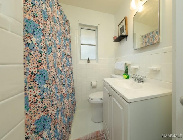 bathroom with a wainscoted wall, toilet, vanity, a shower with curtain, and tile walls