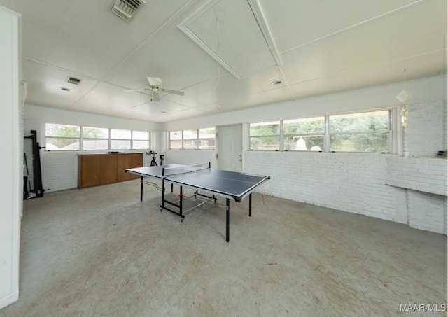 rec room with concrete floors, attic access, visible vents, and brick wall