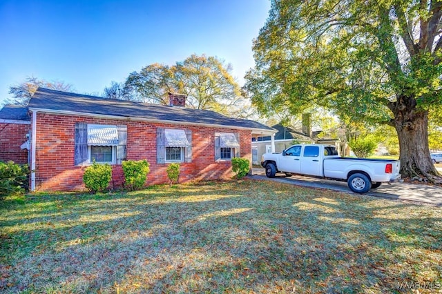 view of front facade with a front yard, brick siding, and a chimney