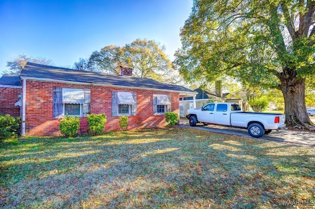 view of front facade with a front yard, brick siding, and a chimney