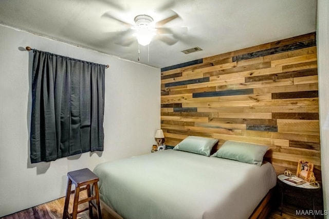 bedroom with a ceiling fan, wood finished floors, visible vents, and wood walls