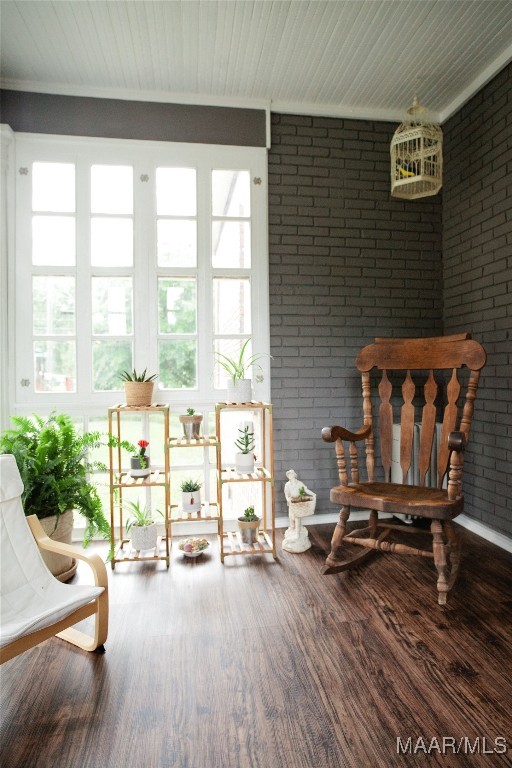 sitting room with plenty of natural light, wood finished floors, and brick wall