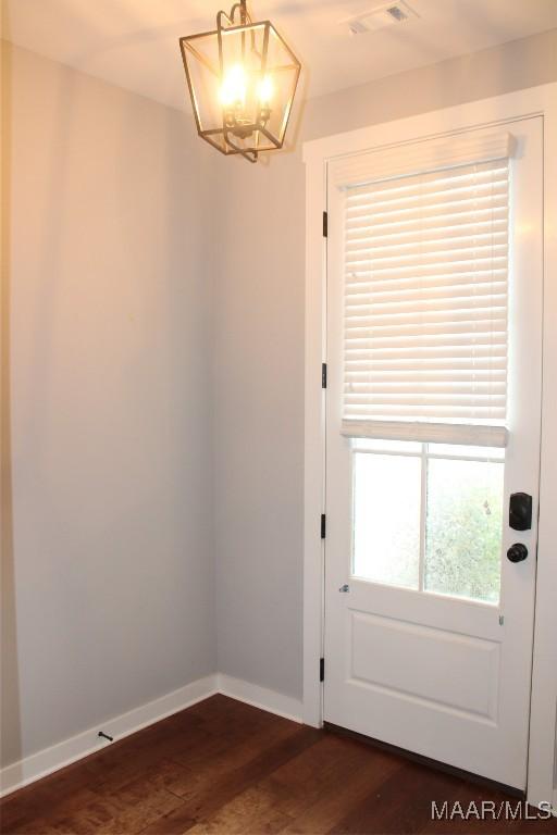 doorway with a notable chandelier, visible vents, baseboards, and dark wood-style flooring