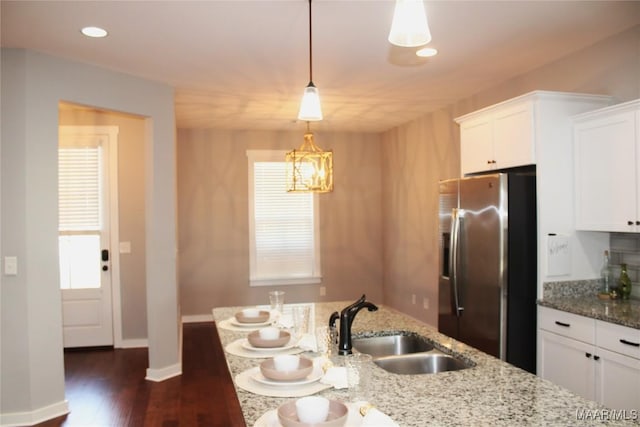 kitchen featuring a sink, stainless steel fridge, light stone counters, and white cabinetry