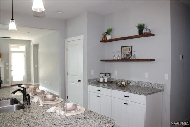 kitchen with light stone countertops, open shelves, a sink, white cabinets, and decorative light fixtures