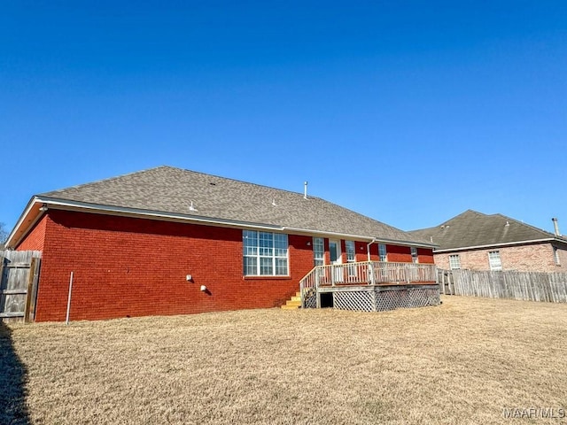 rear view of property featuring fence, a yard, roof with shingles, a wooden deck, and brick siding