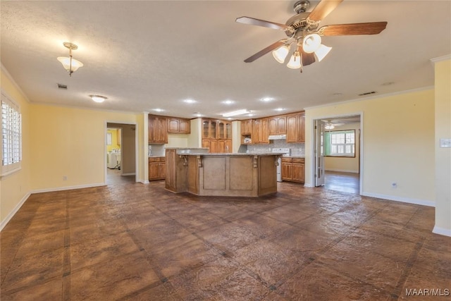 kitchen featuring under cabinet range hood, baseboards, ornamental molding, and a center island