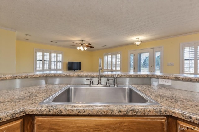 kitchen featuring crown molding, ceiling fan, light countertops, a textured ceiling, and a sink