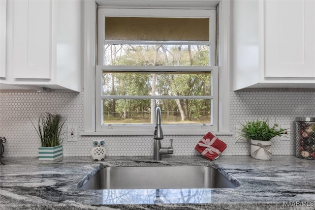 kitchen featuring light stone counters, white cabinetry, and a sink