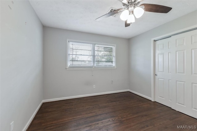 unfurnished bedroom with dark wood-style floors, a closet, baseboards, and a ceiling fan