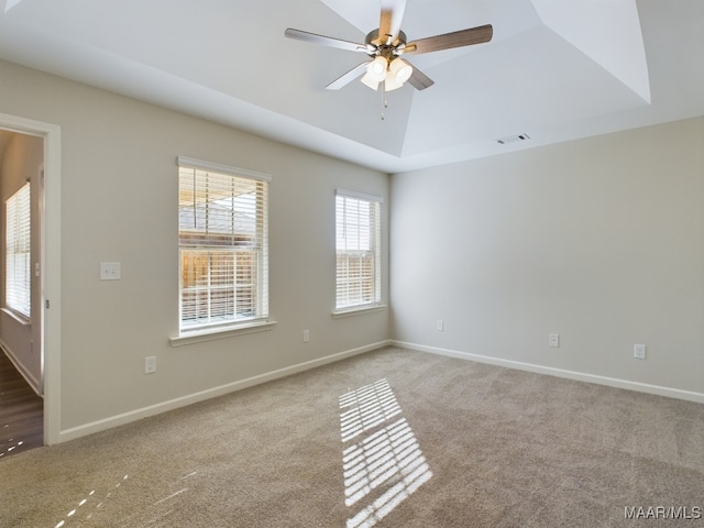 unfurnished room featuring a tray ceiling, visible vents, carpet floors, and ceiling fan