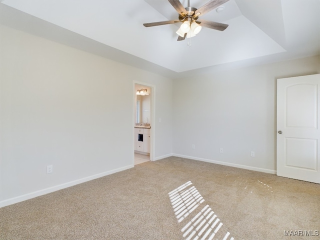 empty room with a ceiling fan, a tray ceiling, light colored carpet, and baseboards