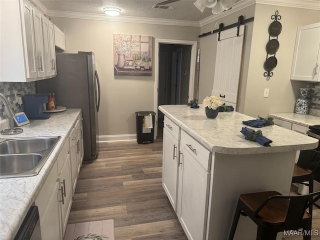 kitchen featuring visible vents, ornamental molding, a sink, a barn door, and a center island