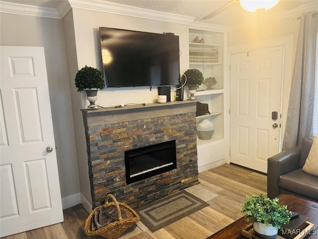 living room featuring a stone fireplace, built in shelves, crown molding, and wood finished floors