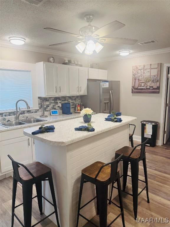 kitchen featuring a breakfast bar area, ornamental molding, a sink, light countertops, and stainless steel refrigerator with ice dispenser