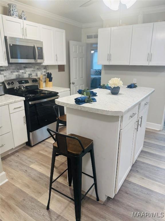 kitchen with light wood finished floors, ornamental molding, stainless steel appliances, white cabinetry, and a kitchen breakfast bar