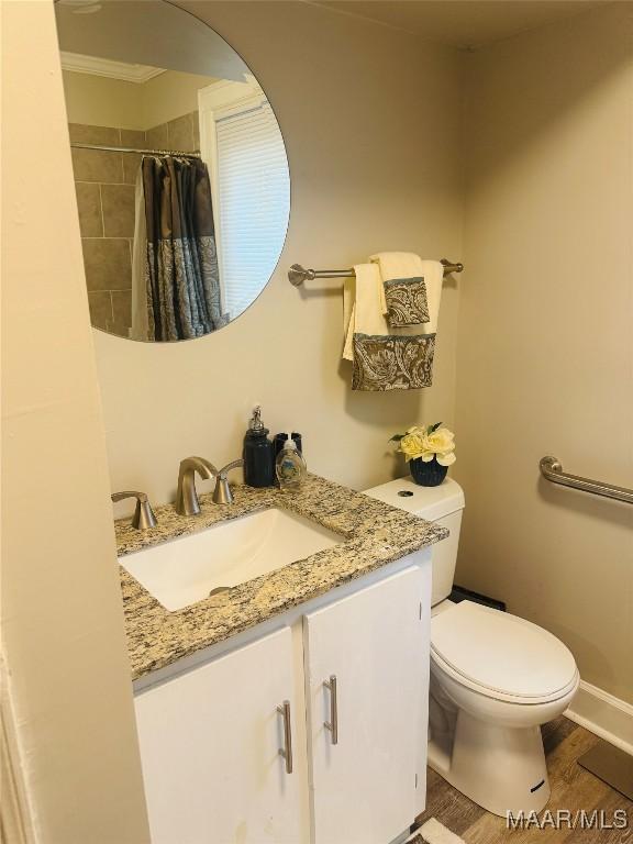 bathroom with toilet, curtained shower, wood finished floors, baseboards, and vanity