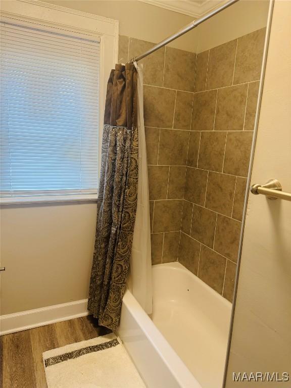 bathroom with wood finished floors, baseboards, and shower / tub combo with curtain