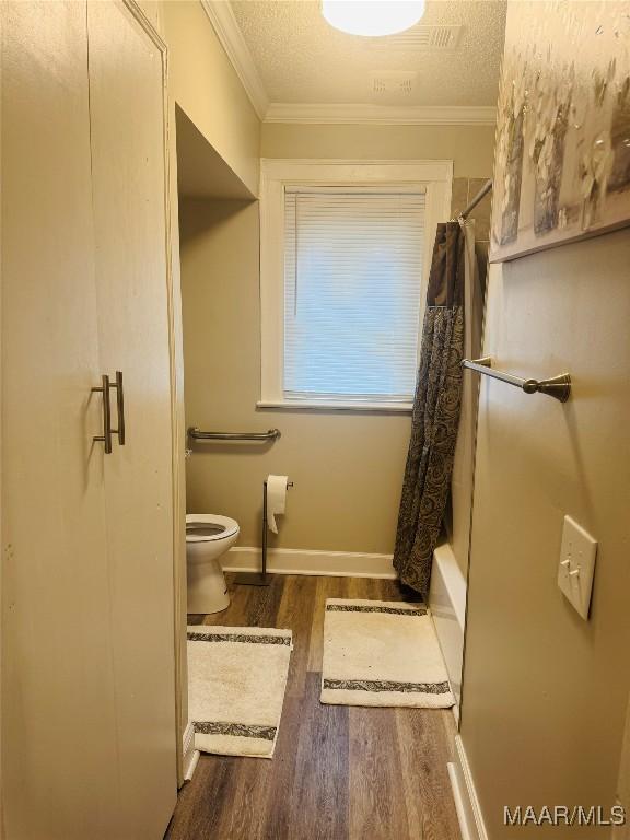 bathroom featuring baseboards, toilet, wood finished floors, and crown molding