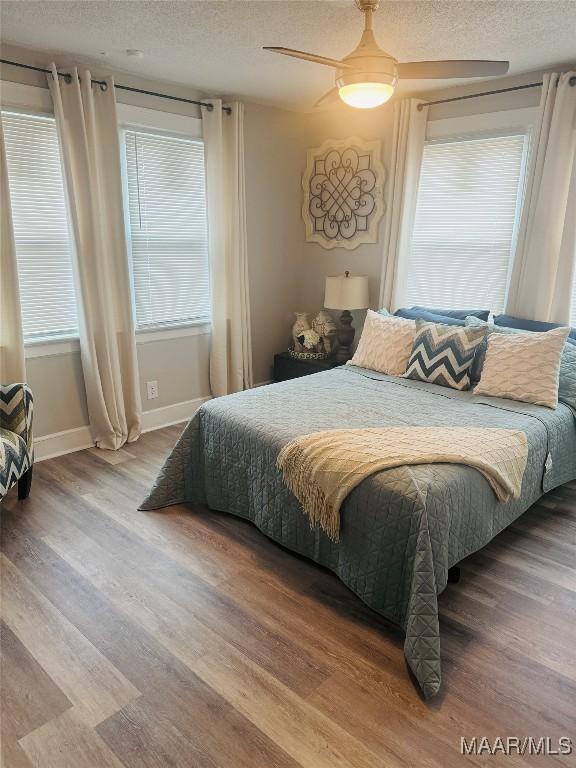 bedroom featuring ceiling fan, baseboards, a textured ceiling, and wood finished floors