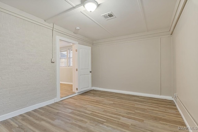 unfurnished room with visible vents, baseboards, light wood-style floors, and brick wall