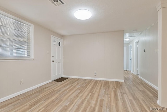 empty room with light wood finished floors, visible vents, and baseboards