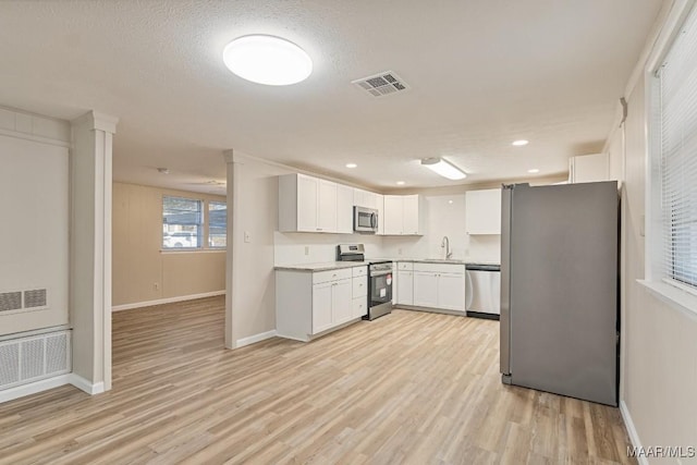 kitchen with visible vents, light wood-style flooring, a sink, stainless steel appliances, and white cabinets