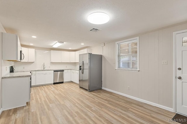 kitchen featuring visible vents, light wood-style floors, white cabinets, stainless steel appliances, and a sink