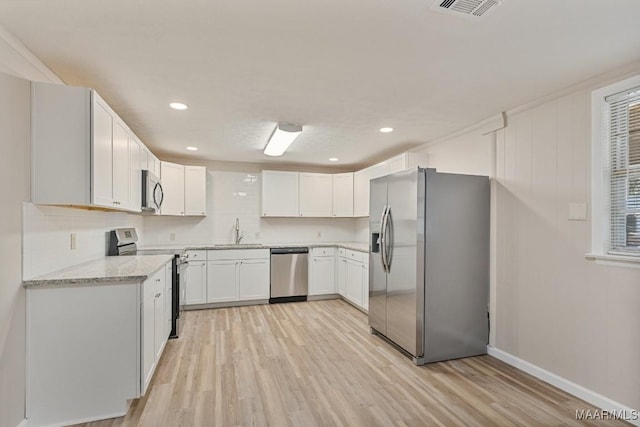 kitchen with light wood finished floors, appliances with stainless steel finishes, tasteful backsplash, and a sink