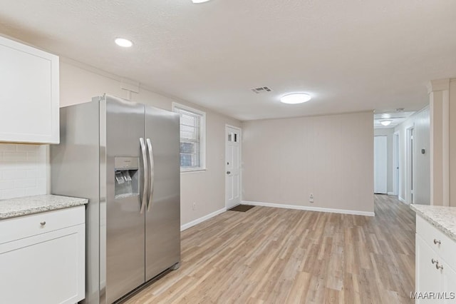 kitchen with light wood-style flooring, visible vents, stainless steel fridge, and white cabinets