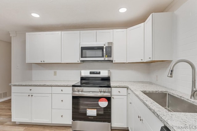 kitchen with light wood finished floors, backsplash, appliances with stainless steel finishes, and a sink