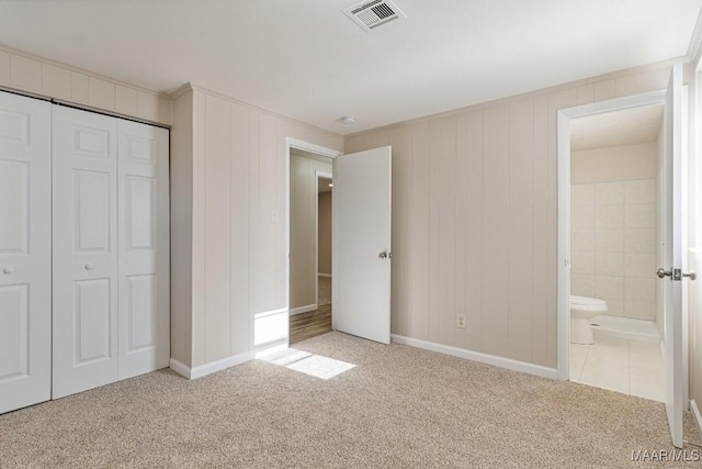 unfurnished bedroom with ensuite bath, a closet, visible vents, and carpet floors