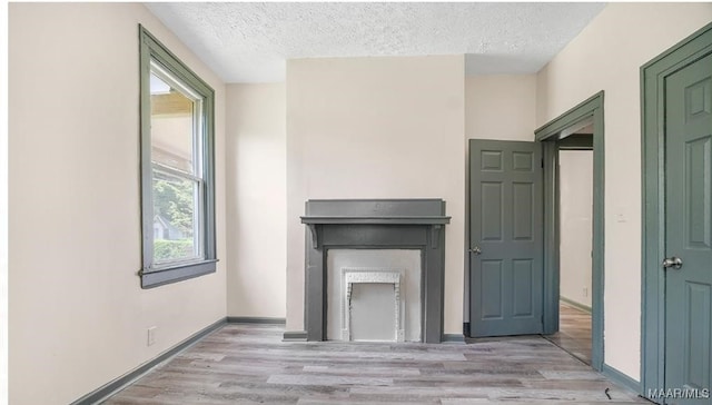 unfurnished living room featuring baseboards, a textured ceiling, wood finished floors, and a fireplace