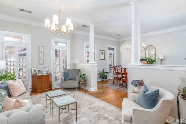 living room with visible vents, crown molding, wood finished floors, a notable chandelier, and ornate columns