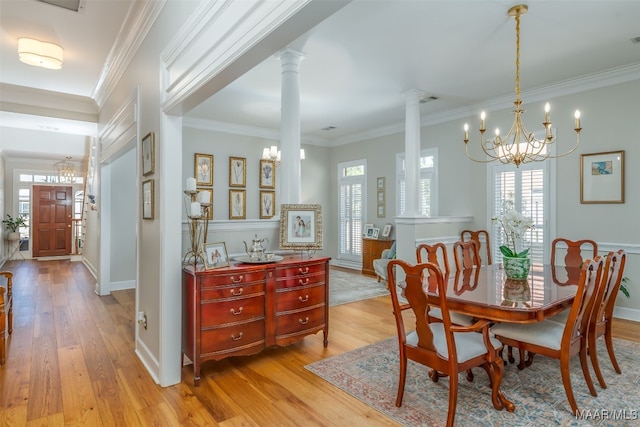 dining room featuring light wood-style flooring, an inviting chandelier, crown molding, and ornate columns