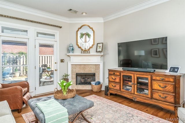 living area with crown molding, wood finished floors, visible vents, and a tile fireplace